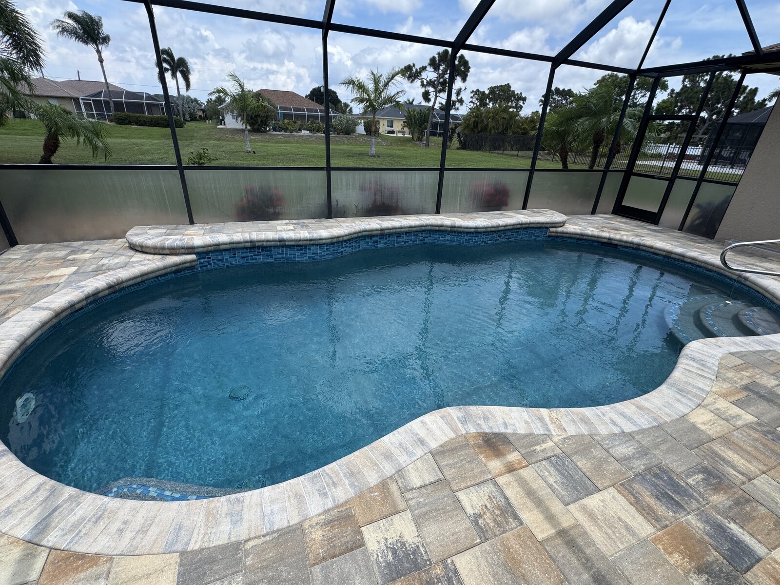 Recent screened-in backyard pool with blue water, tile, coping, and paver deck